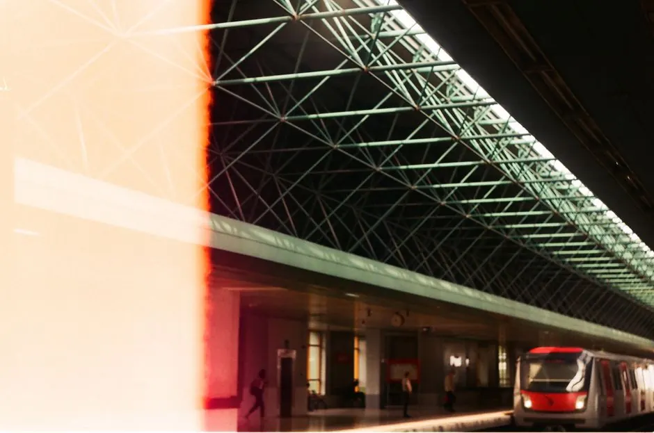 A contemporary train station features a geometric roof with a train arriving on the platform.