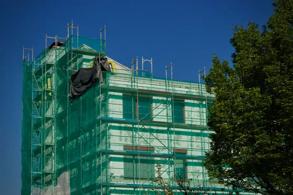 Building under renovation covered with green scaffolding against a clear blue sky.