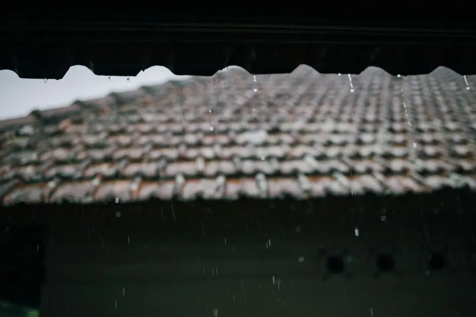 Close-up of a tiled roof with rain drops falling, capturing the moody ambiance of a rainy day.